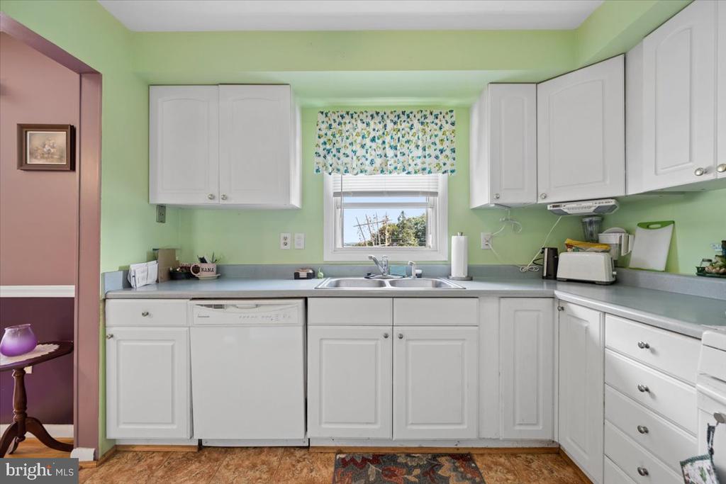Kitchen with white cabinets, pale green walls, and a sink beneath a window with a floral valance.