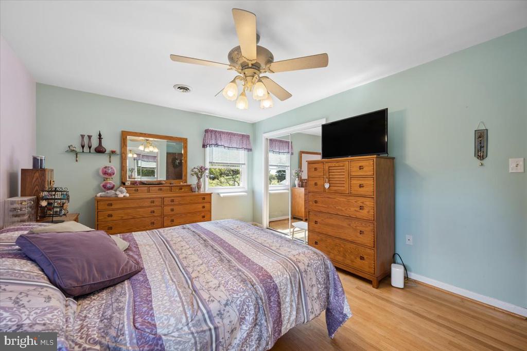 Bedroom with a purple patterned bedspread, matching wooden dressers, and a ceiling fan.