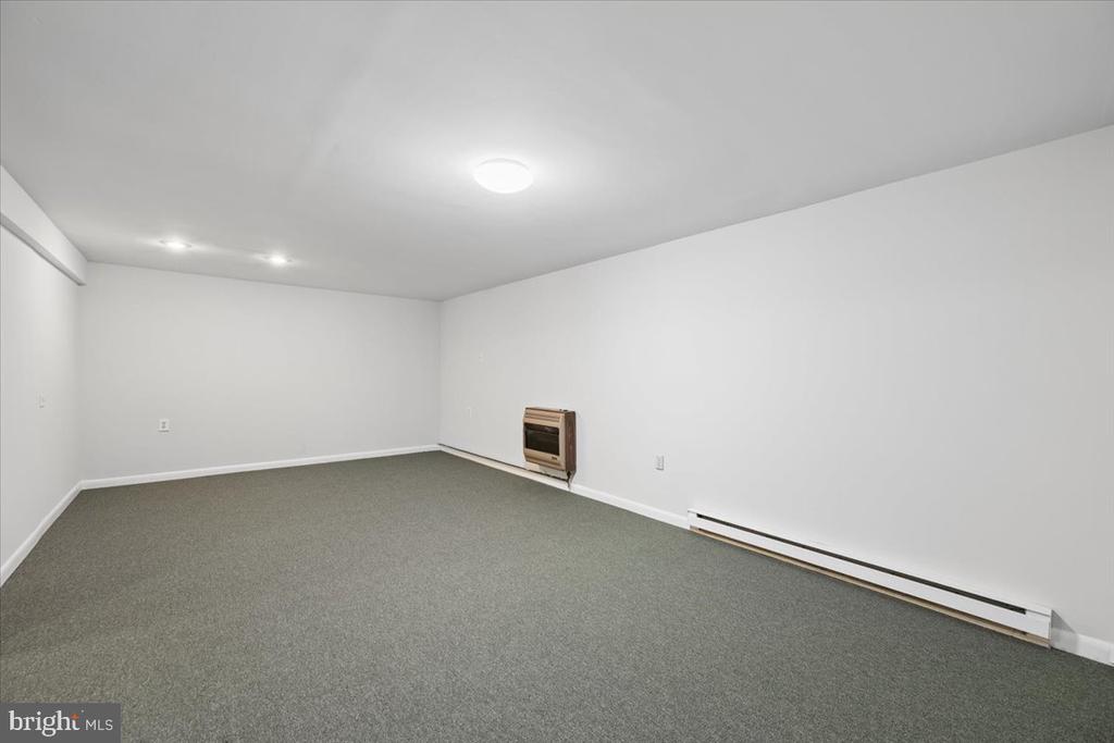 Empty carpeted room with white walls, a wall-mounted heater, and baseboard heating.