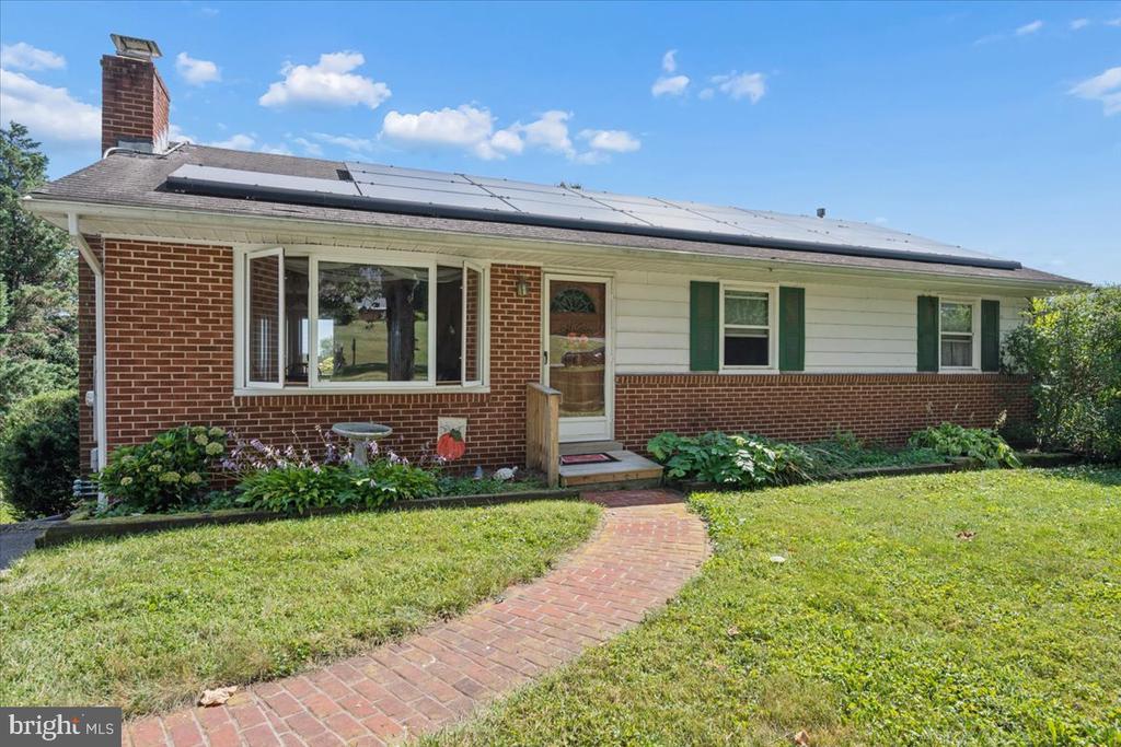 Single-story brick house with rooftop solar panels and a curved brick walkway through the front lawn.