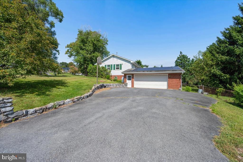 Home with a broad paved driveway, brick-front garage, and solar panels.