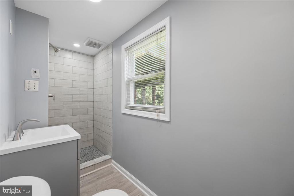 Bathroom with a tiled walk-in shower, gray vanity, and window with blinds.