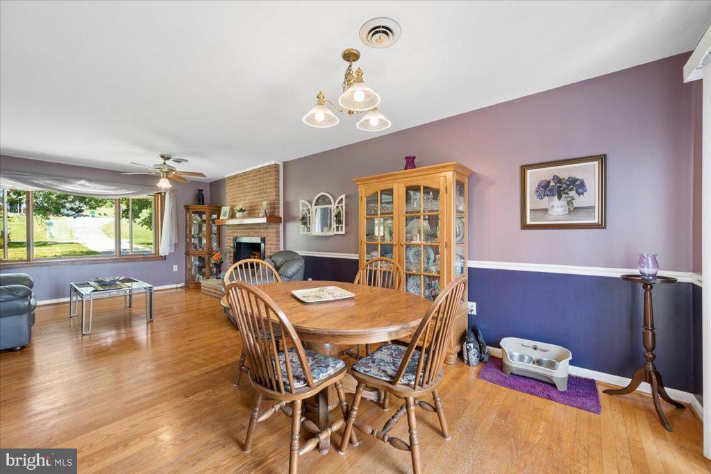 Dining area with a wooden table, glass-front china cabinet, brick fireplace, and hardwood floors.