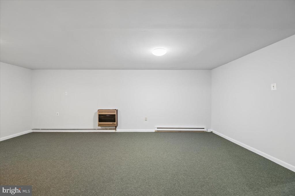 Empty carpeted room with a wall-mounted heater and baseboard heating.