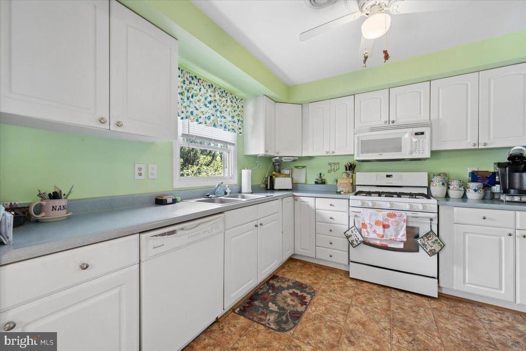 Kitchen with white cabinets, pale green walls, and a white gas range beneath a microwave.