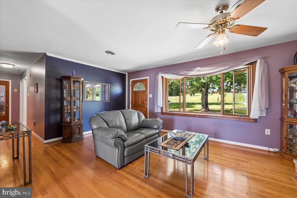 Living room with a gray leather sofa, hardwood floors, and a large window overlooking a green yard.