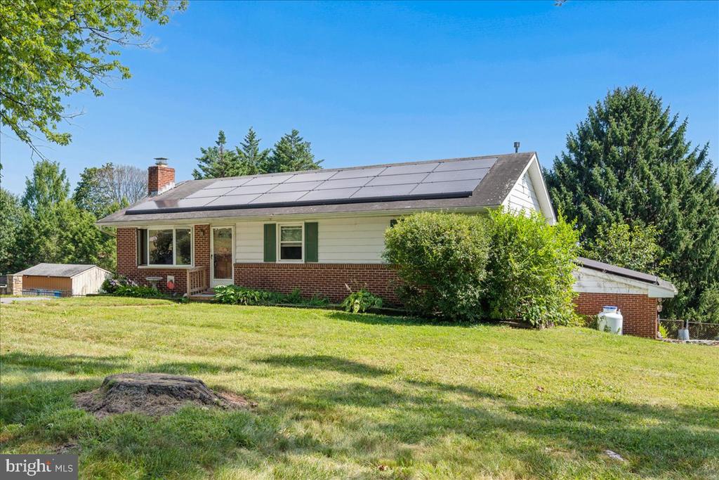 Single-story brick-and-siding home with rooftop solar panels on a broad lawn.
