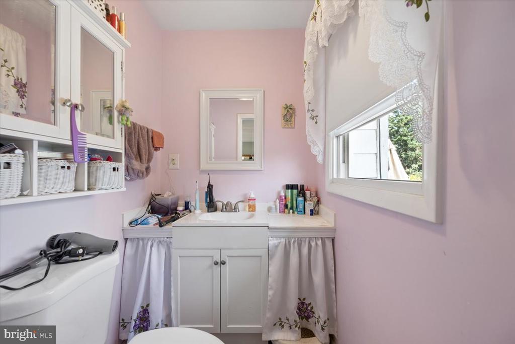 Bathroom with a white vanity, pink walls, lace curtains, and mirrored storage shelves.