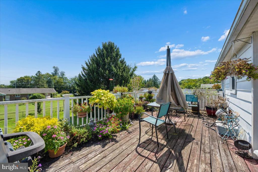 Wooden deck with patio seating, a closed umbrella, and colorful potted flowers along the railing.