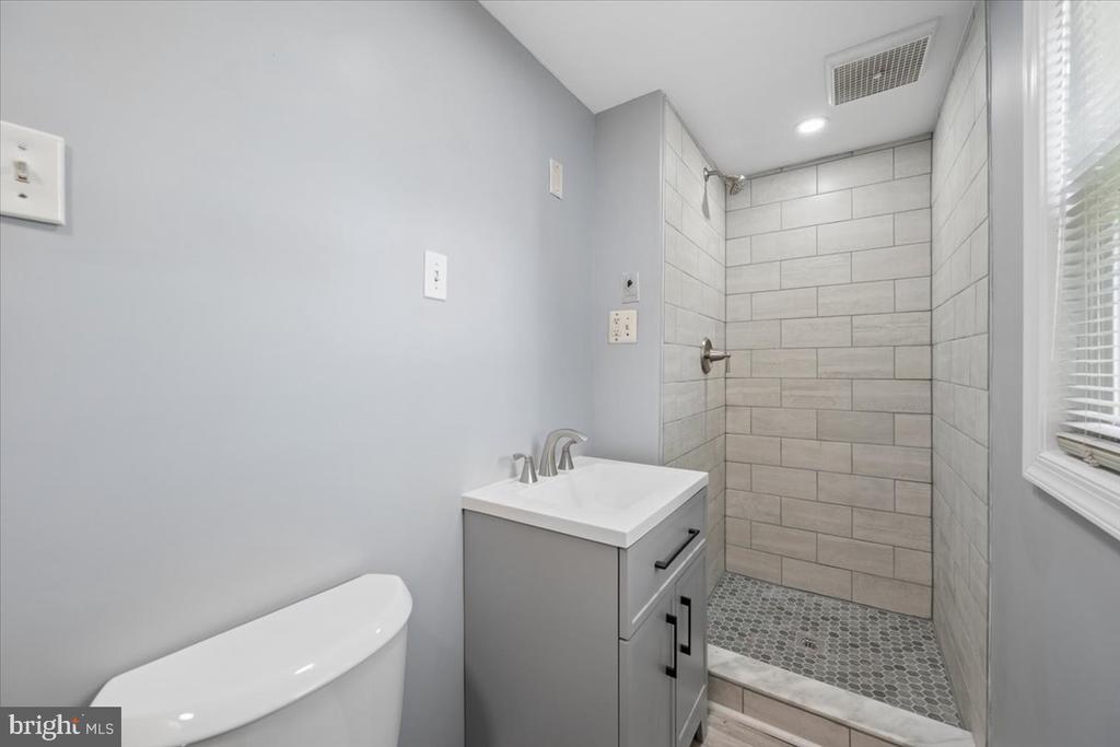 Bathroom with a walk-in tiled shower, gray vanity, modern toilet, and window with white blinds.