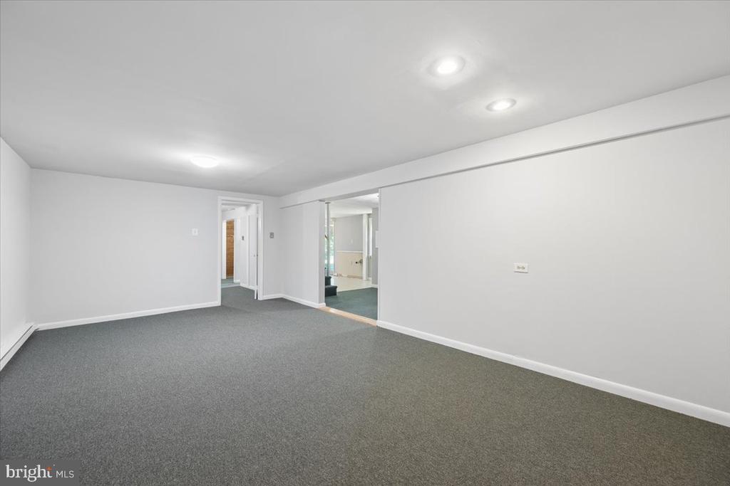 Empty carpeted room with recessed lights and doorways to adjoining spaces.
