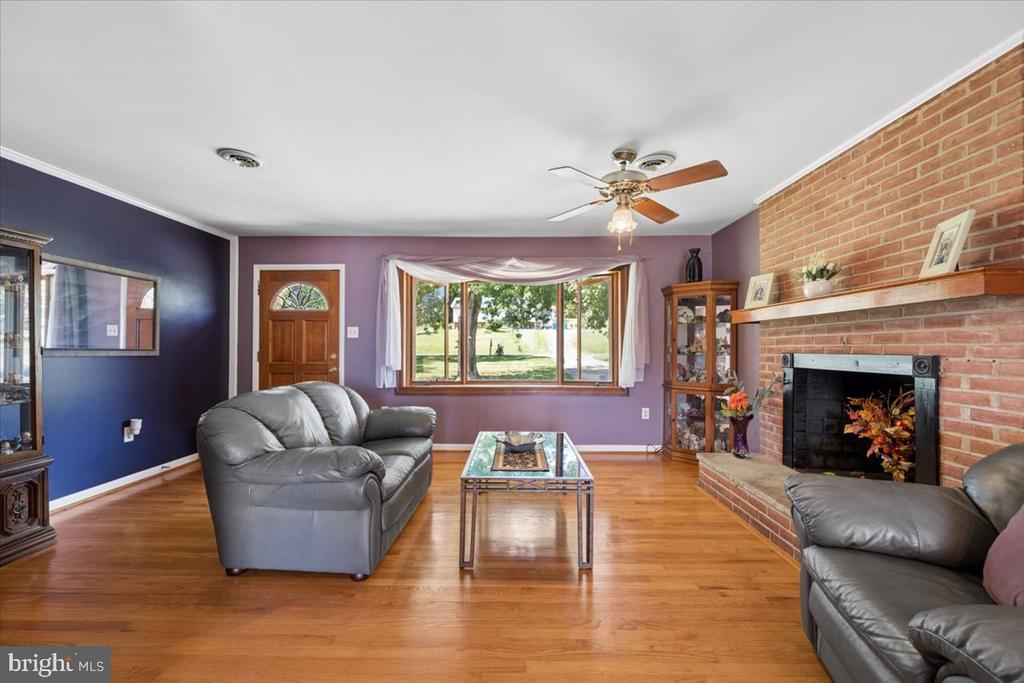Living room with a brick fireplace, hardwood floors, gray leather sofas, and a wide window.