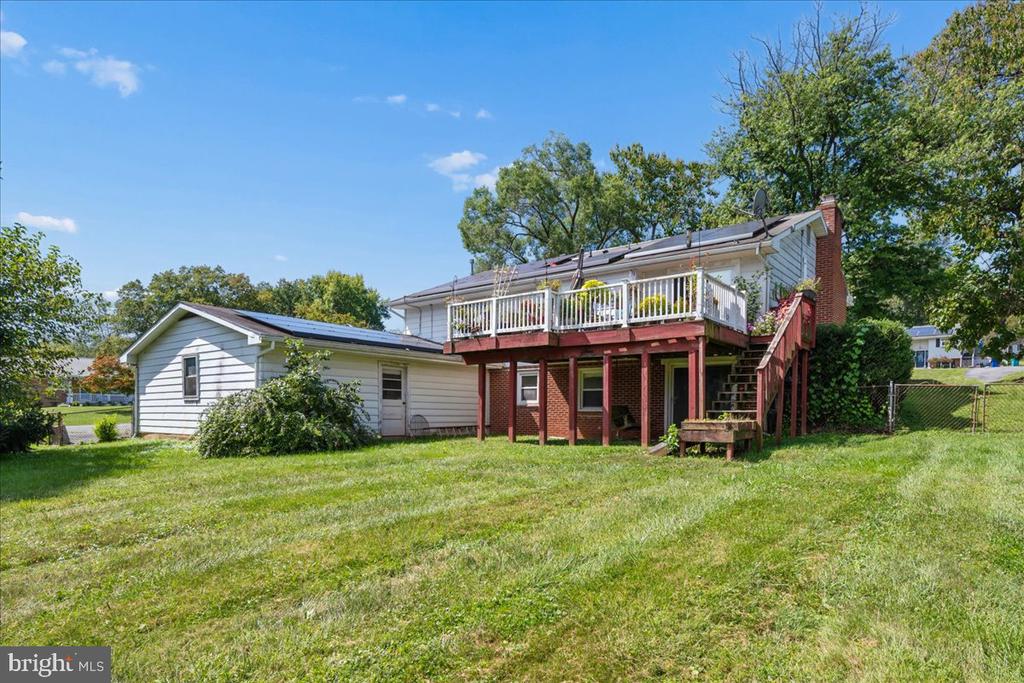 Rear of a house with a raised deck, exterior stairs, rooftop solar panels, and a broad lawn.