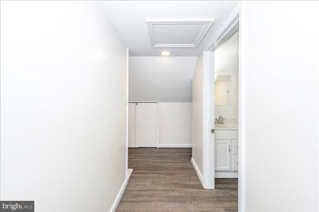 Empty hallway with wood-look flooring, ceiling access hatch, and an open bathroom doorway.