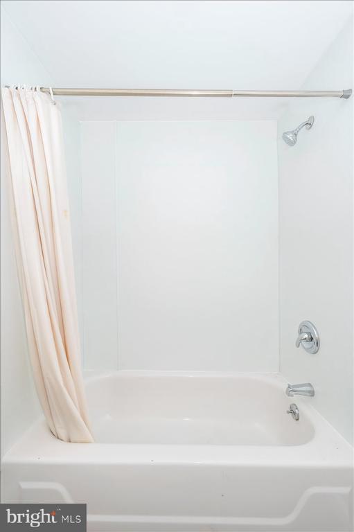 Bathroom bathtub and shower with a pale curtain and chrome fixtures.