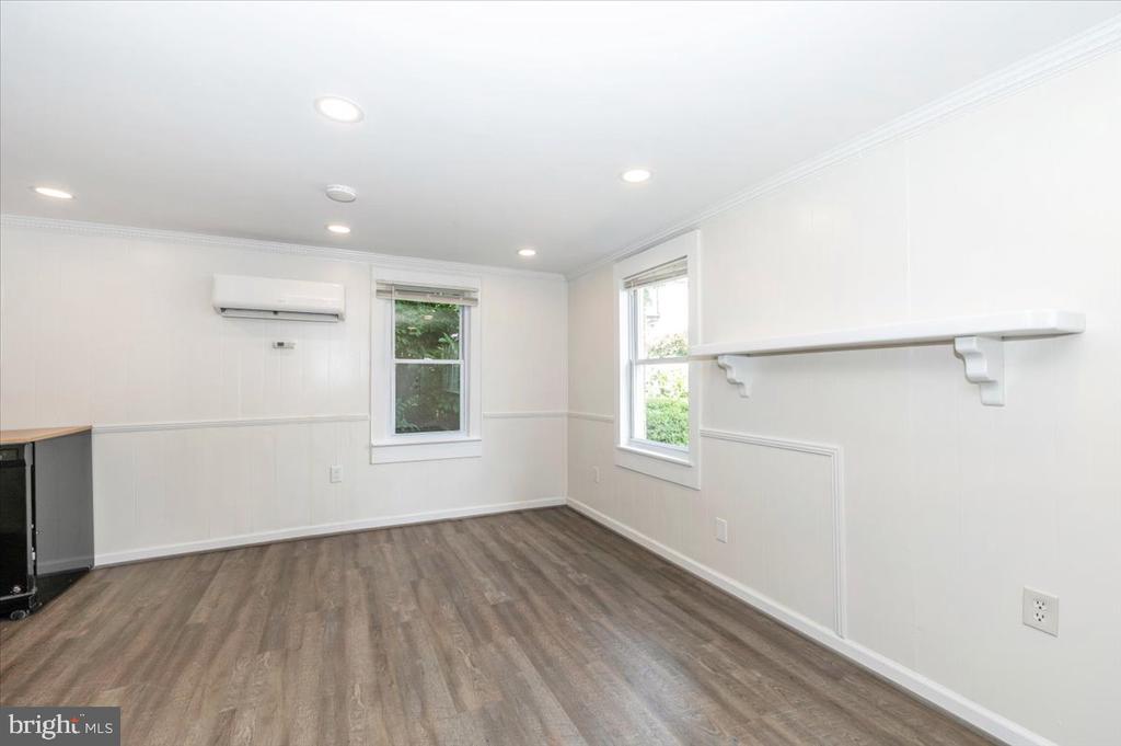 Empty room with wood-look flooring, two windows, a wall-mounted mini-split, and a long white shelf.