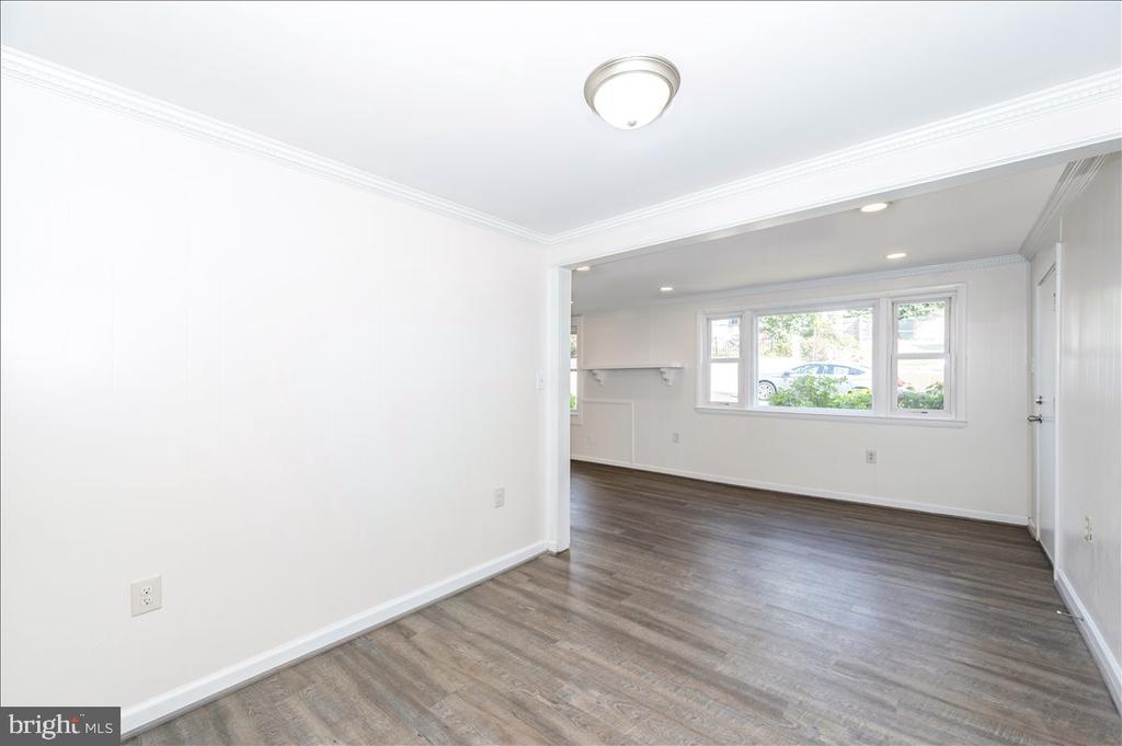 Vacant room with plank flooring and crown molding, opening to a bright room with a wide window.