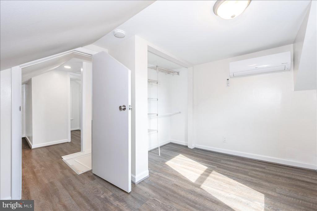 Vacant bedroom with an open closet, gray flooring, and a wall-mounted mini-split air conditioner.