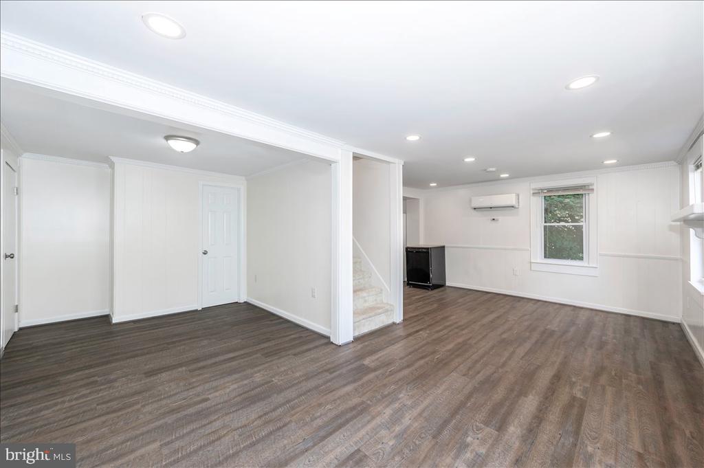 Empty interior room with brown flooring, white walls, a staircase, and a wall-mounted air conditioner.