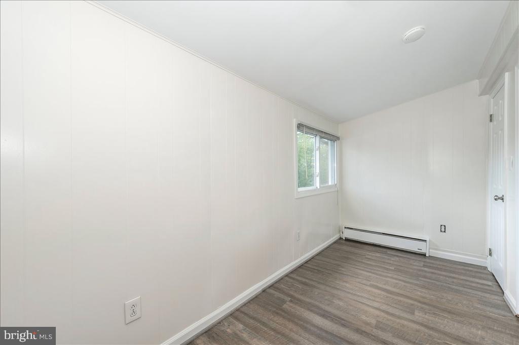 Empty room with white paneled walls, plank flooring, a window, and a baseboard heater.