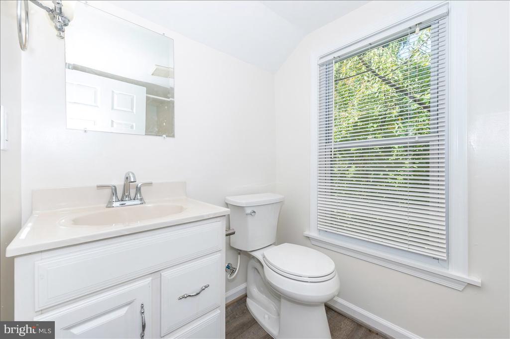 Bright bathroom with a white vanity, toilet, and large window with blinds.