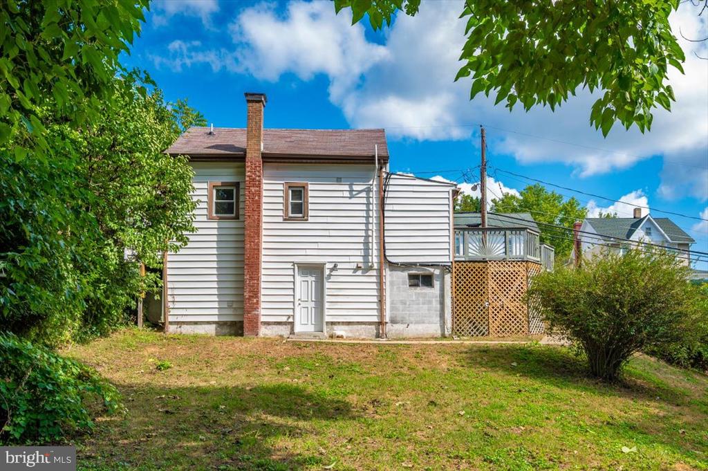 Rear of a white-sided house with a brick chimney, raised deck, and grassy yard.