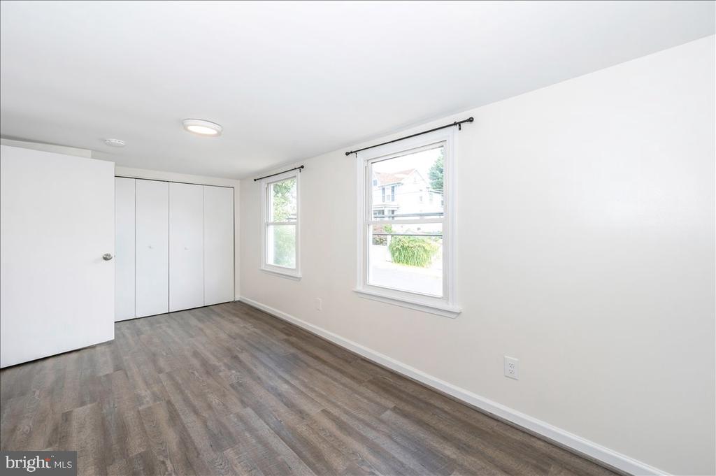 Empty room with a built-in closet, two windows, and gray-brown plank flooring.