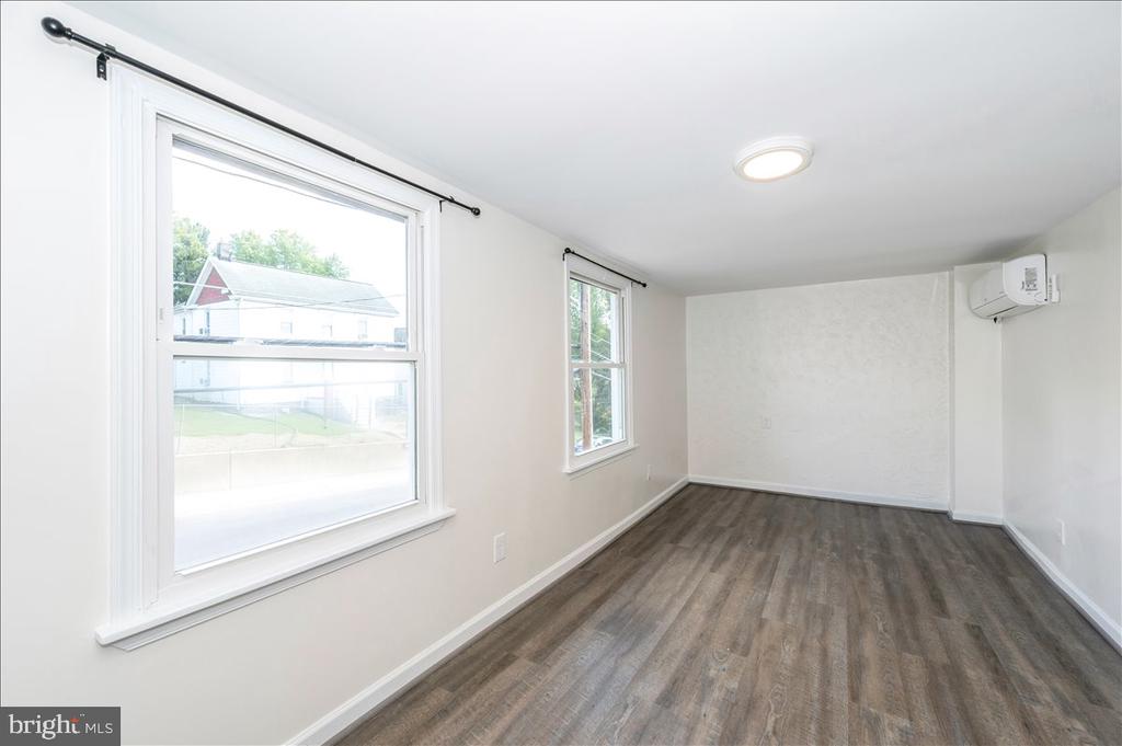 Vacant room with dark wood-look floors, two windows, and a wall-mounted air conditioner.