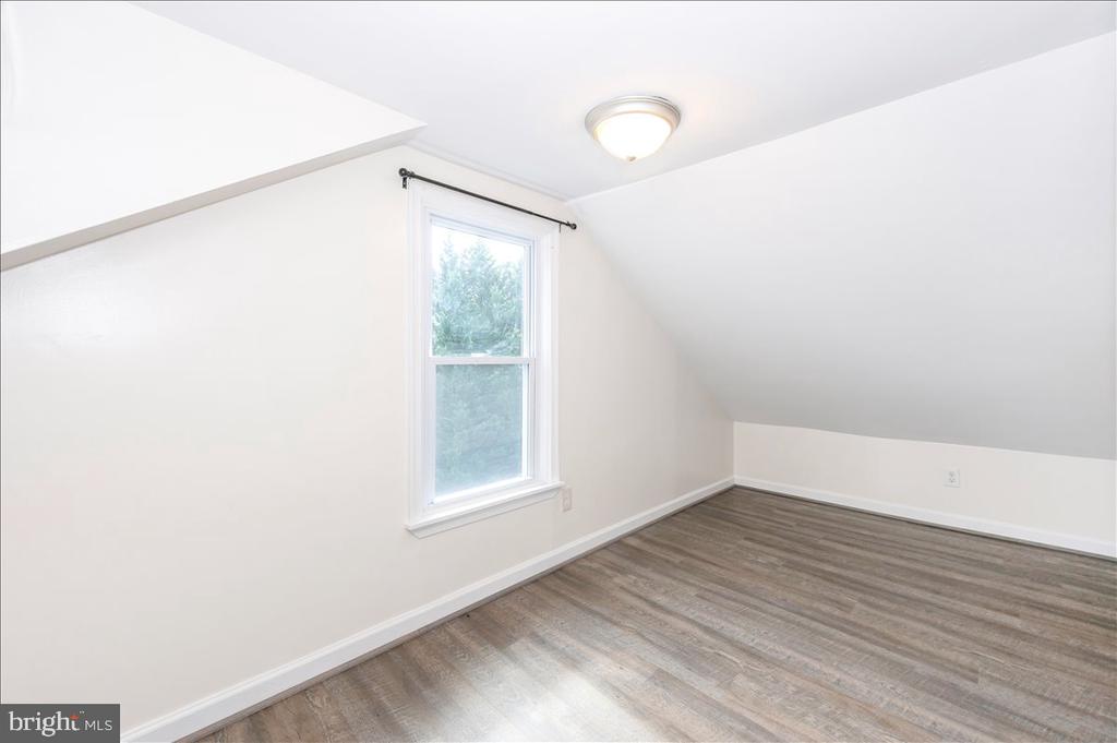 Empty upper-floor room with a sloped ceiling, single window, and gray-brown plank flooring.