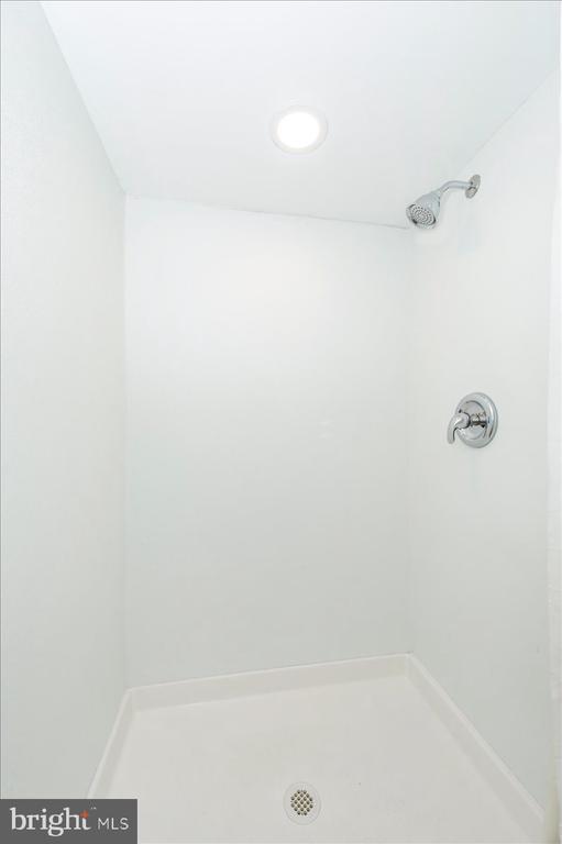 White shower stall with chrome fixtures, recessed ceiling light, and floor drain.