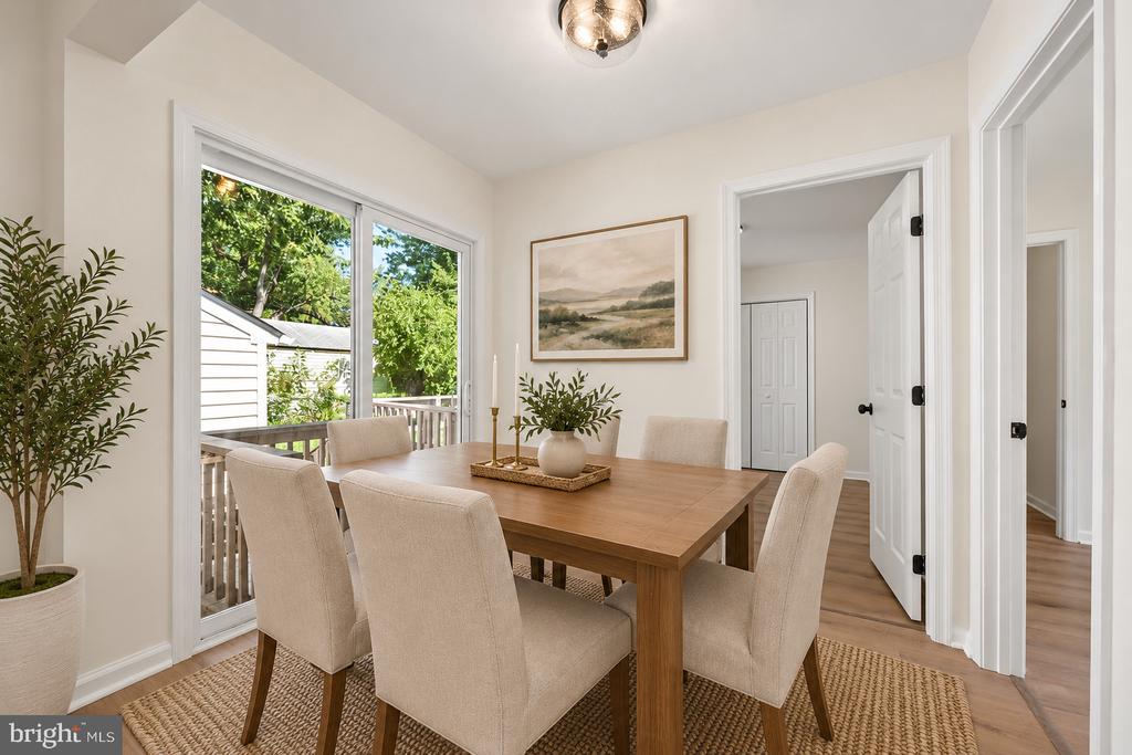 Dining room with a wood table and upholstered chairs beside sliding glass doors overlooking leafy trees.