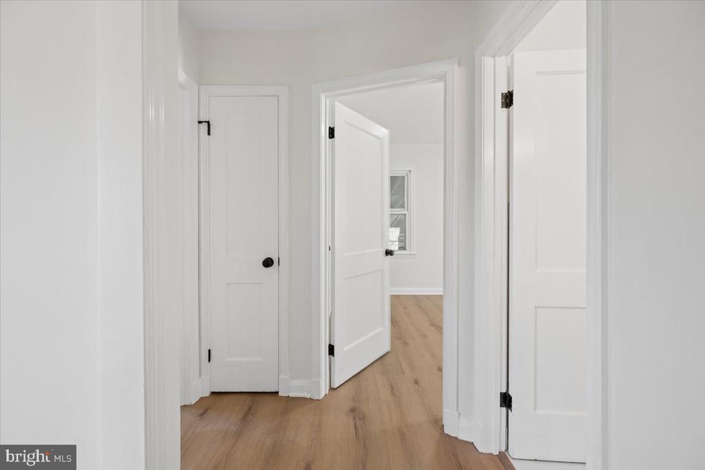 Empty hallway with light wood flooring and multiple white paneled doors.