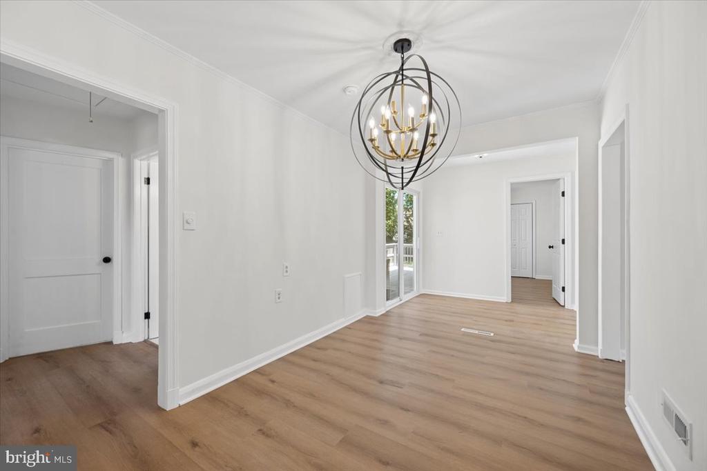 Empty interior room with light wood floors, a spherical chandelier, and glass doors to a deck.