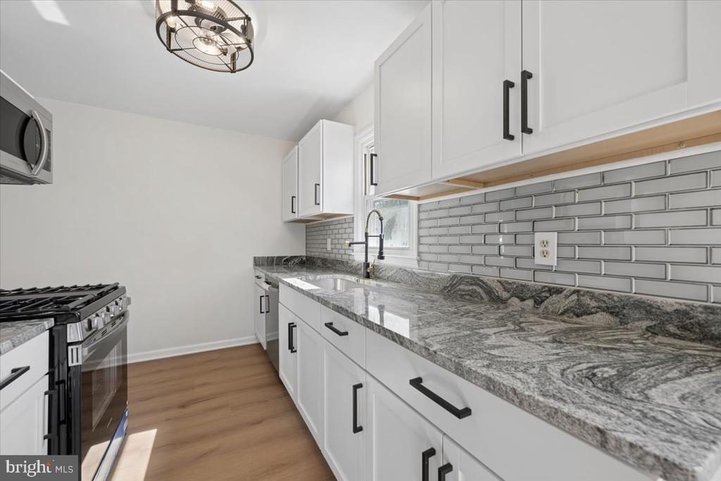 Kitchen with white cabinets, gray stone counters, subway tile backsplash, and a stainless steel range.