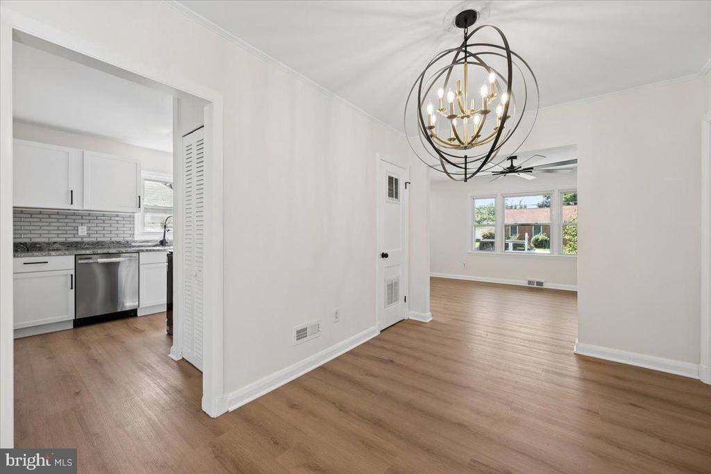 Open living and dining area with wood-look floors, a globe chandelier, and an adjoining white kitchen.
