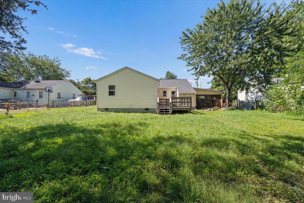 Rear of a pale yellow home with a raised deck and a large grassy backyard.