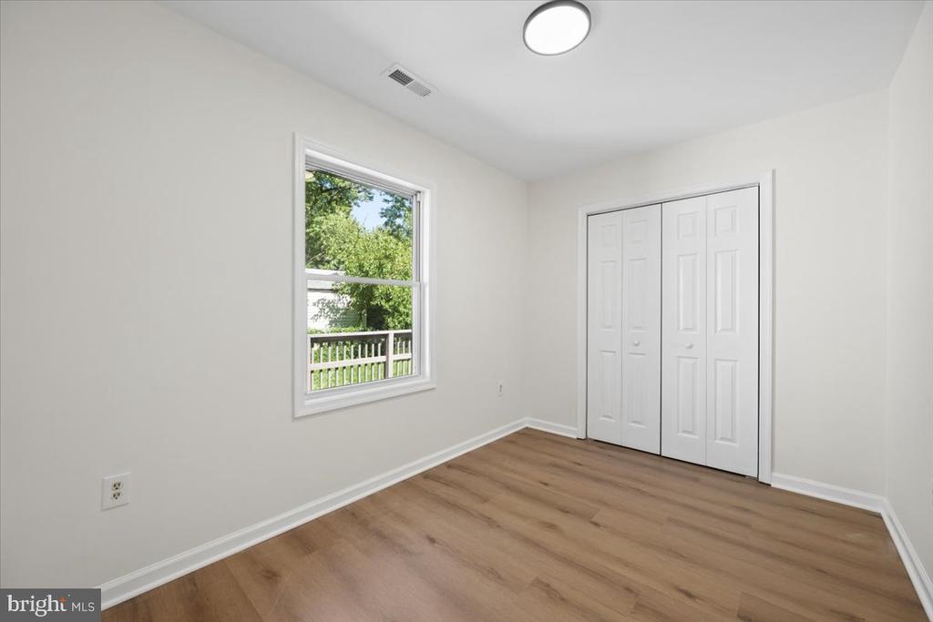 Empty bedroom with wood-look flooring, a window overlooking greenery, and a white double-door closet.