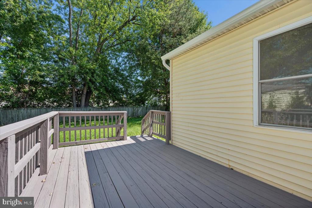 Spacious gray deck beside a yellow-sided house, overlooking a fenced, tree-shaded backyard.