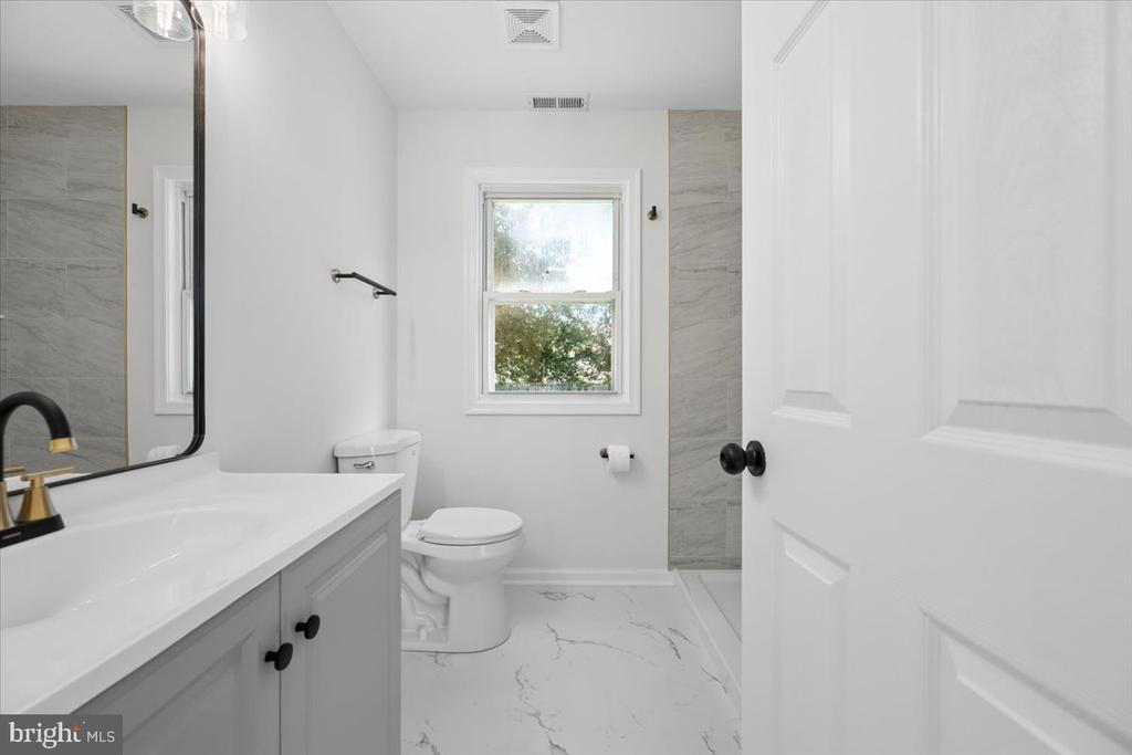 Bathroom with a gray vanity, black faucet, tiled shower, and window.