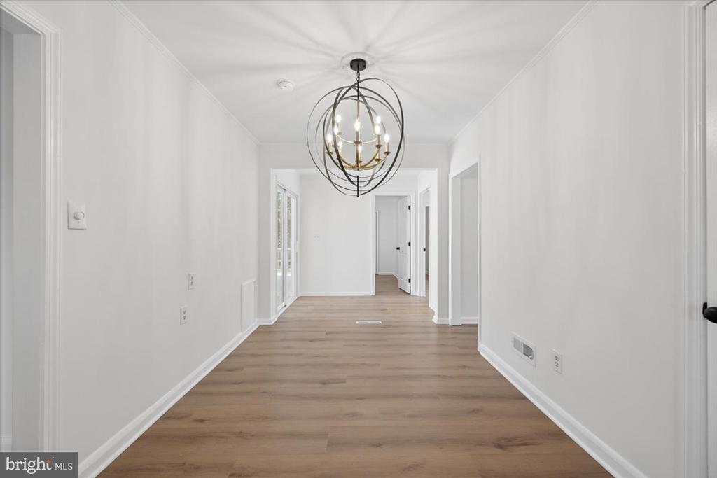 Empty hallway with light wood-look flooring and a spherical chandelier.