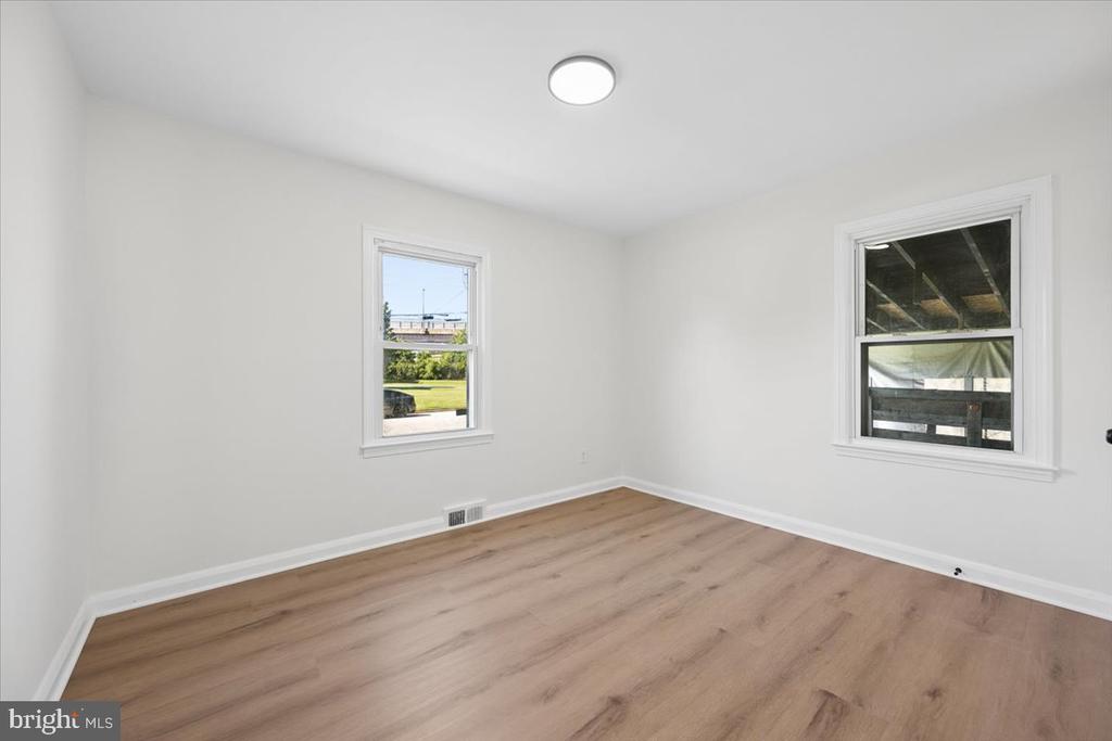 Empty room with light wood-look flooring, white walls, and two windows.