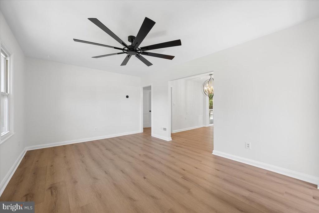 Vacant living room with light wood floors and a large black ceiling fan.