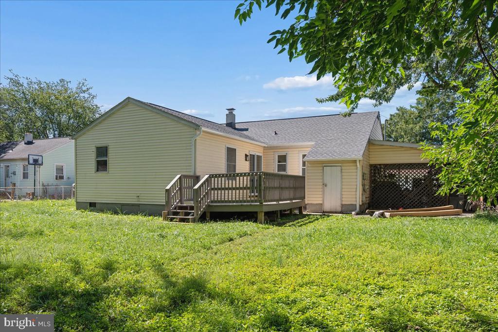 Rear of a single-story house with a raised wooden deck, covered patio, and broad grassy lawn.