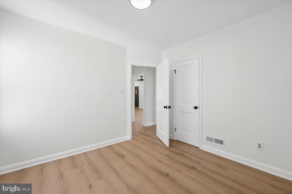 Empty room with light wood flooring, white walls, and an open door to the hallway.