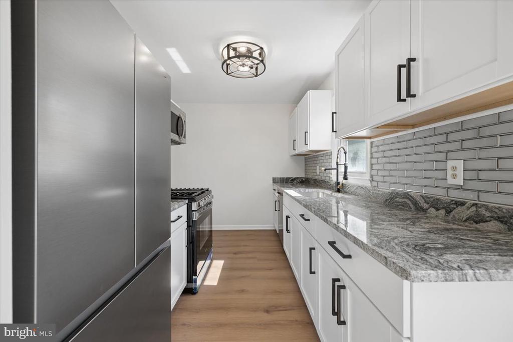 Renovated kitchen with white cabinets, stone counters, gray tile backsplash, and stainless-steel appliances.
