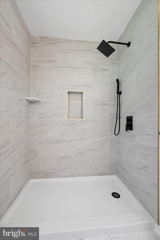Walk-in shower with gray marble-look tile, matte black fixtures, recessed niche, and white base.