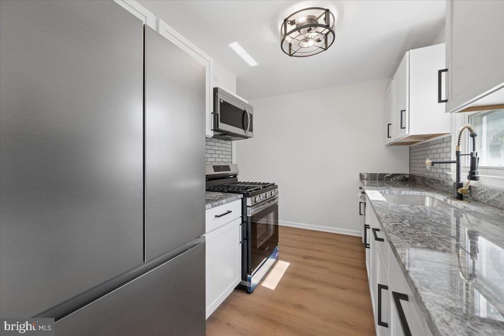 Renovated kitchen with white cabinets, gray stone counters, stainless steel appliances, and wood-look flooring.