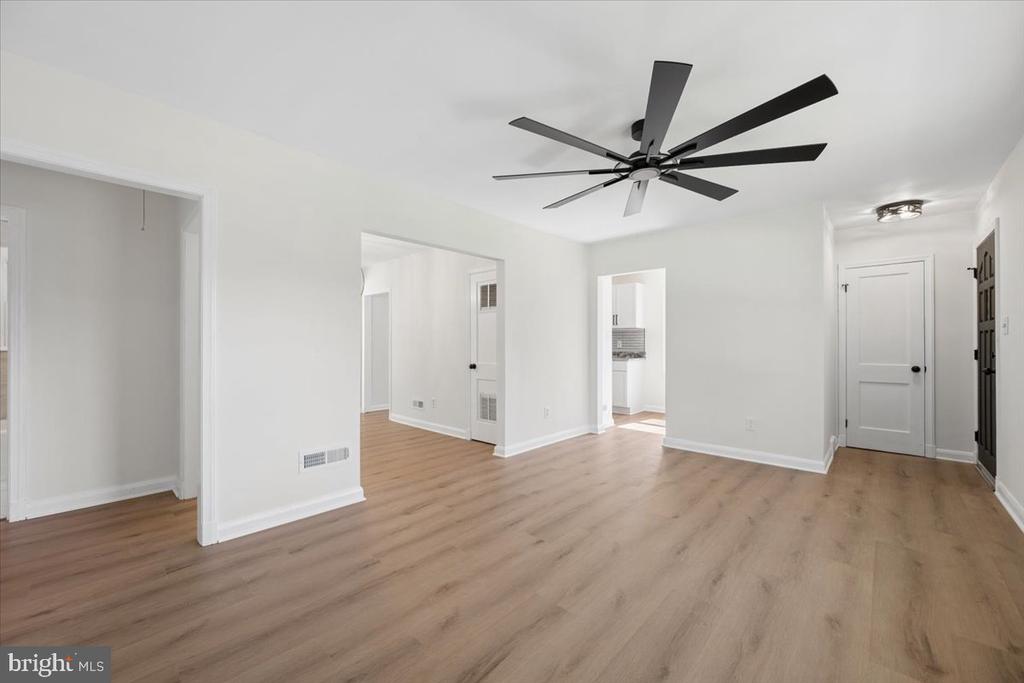 Vacant room with light wood floors, white walls, and a black ceiling fan.