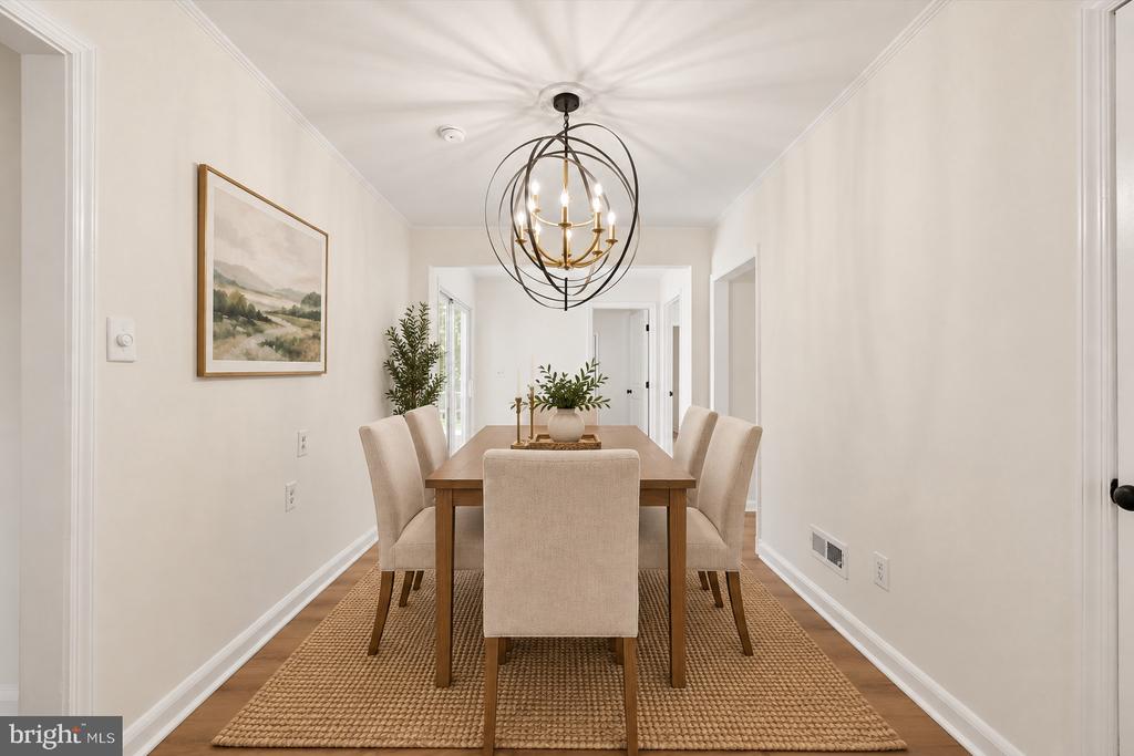 Dining room with a wood table, upholstered chairs, woven rug, and spherical chandelier.