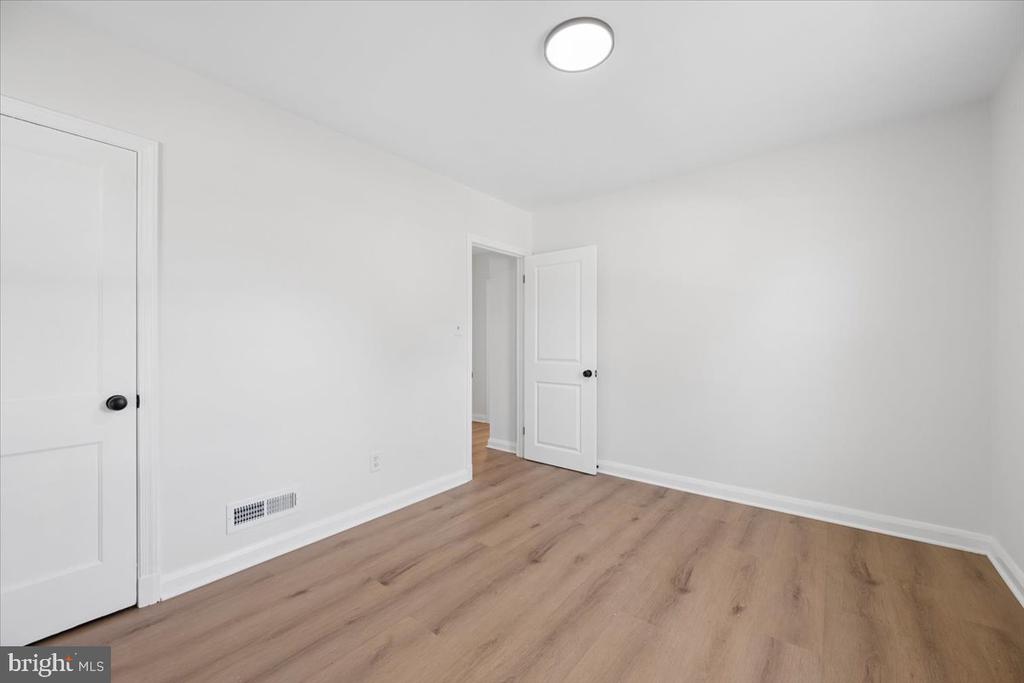 Empty room with light wood-look flooring, white walls, and two doors.